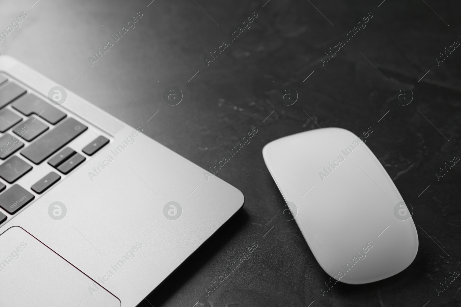 Photo of Wireless mouse and laptop on dark textured table, closeup