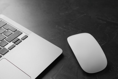 Wireless mouse and laptop on dark textured table, closeup