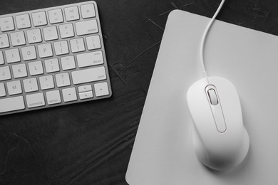 Wired mouse with mousepad and computer keyboard on dark textured table, flat lay