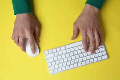 Photo of Man working with mouse and computer keyboard at yellow table, top view