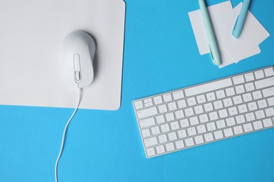 Wired mouse with mousepad, stationery and computer keyboard on light blue background, flat lay