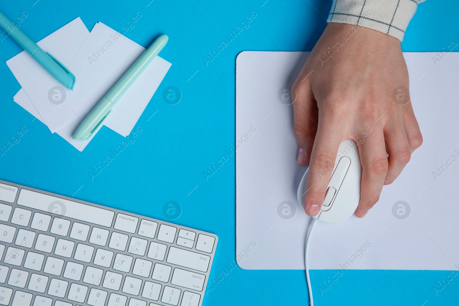 Photo of Man working with mouse, computer keyboard and stationery at light blue table, top view