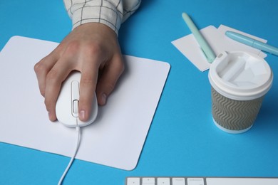 Man with mouse, paper cup and stationery at light blue table, closeup