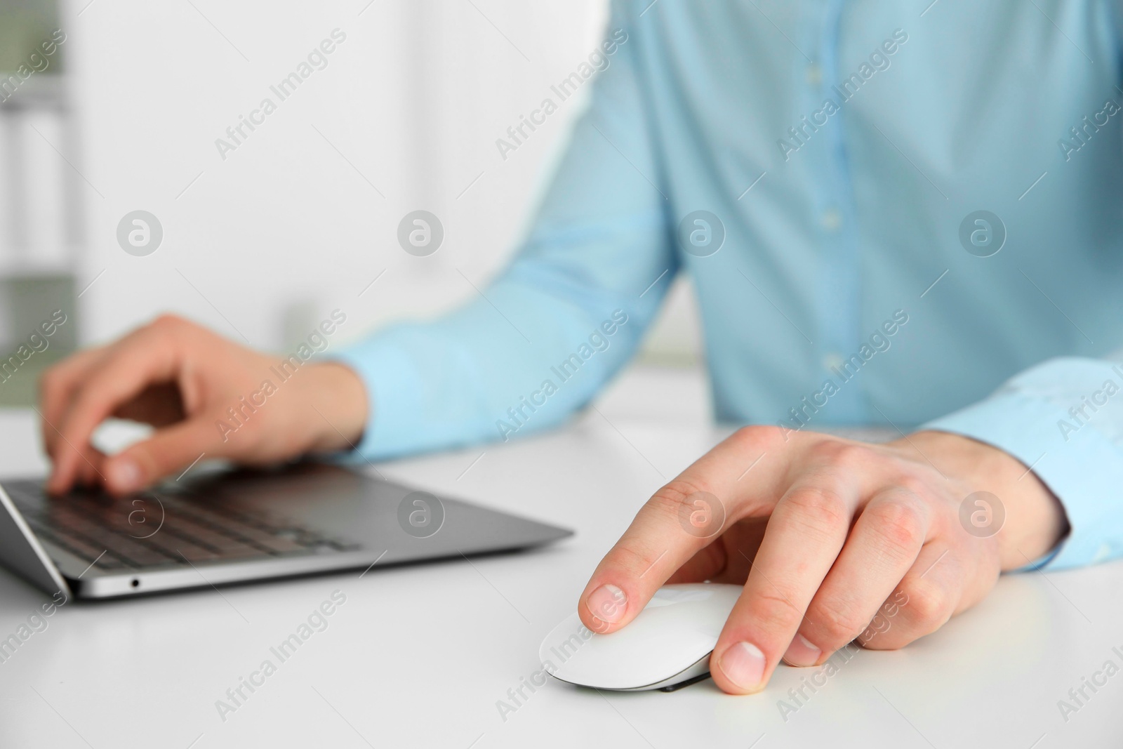 Photo of Man working with wireless mouse and laptop at white table indoors, closeup