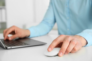 Man working with wireless mouse and laptop at white table indoors, closeup