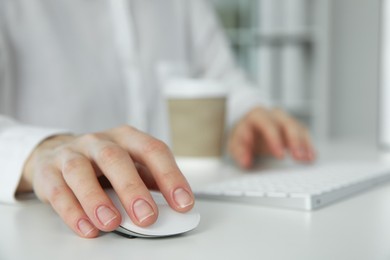 Photo of Woman with wireless mouse and paper cup at white table indoors, closeup