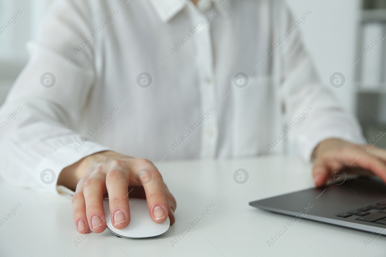 Photo of Woman working with wireless mouse and laptop at white table indoors, closeup