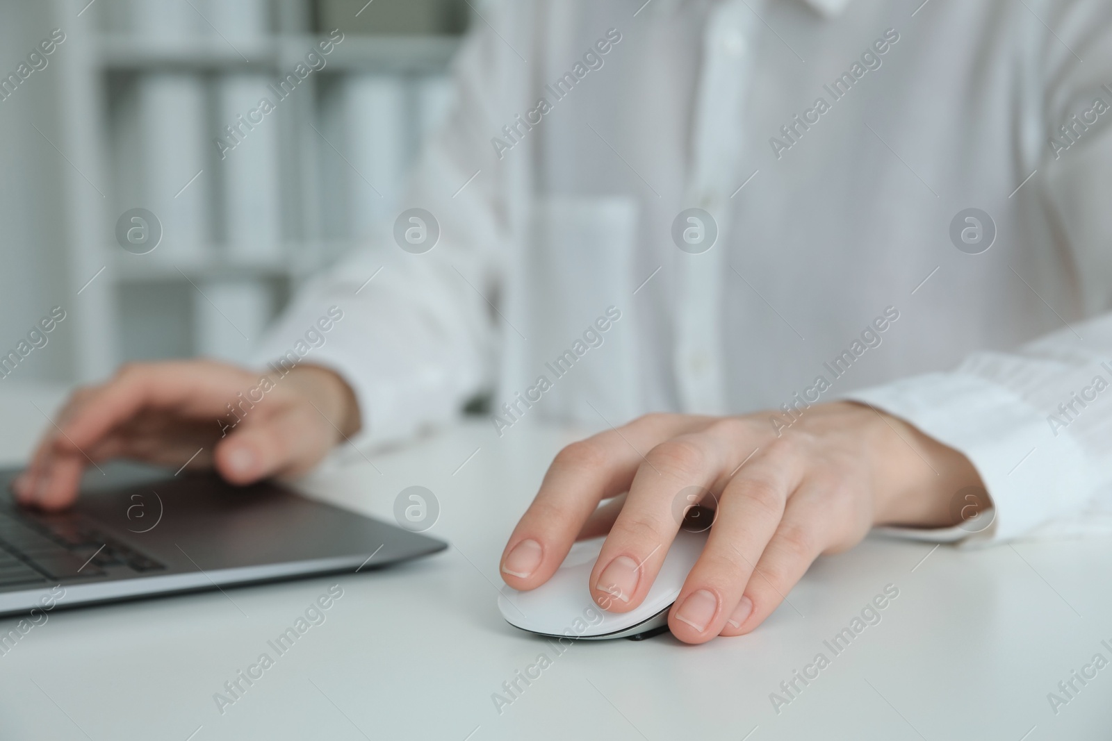 Photo of Woman working with wireless mouse and laptop at white table indoors, closeup