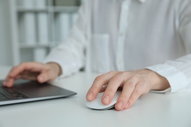 Woman working with wireless mouse and laptop at white table indoors, closeup