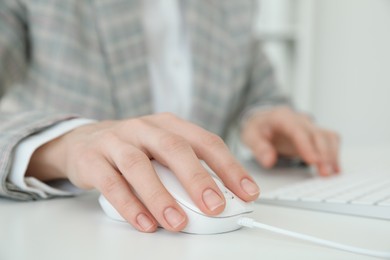 Photo of Woman working with wired mouse and computer keyboard at white table indoors, closeup