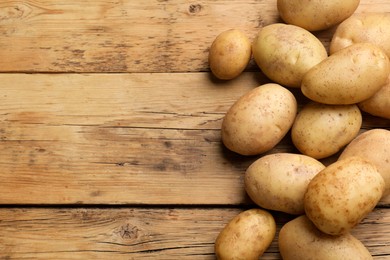 Photo of Many fresh potatoes on wooden table, top view. Space for text