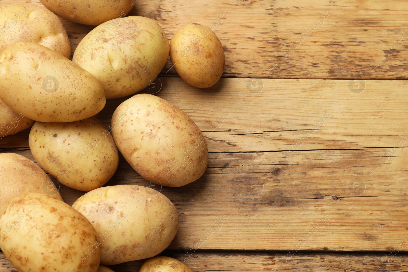 Photo of Many fresh potatoes on wooden table, top view. Space for text