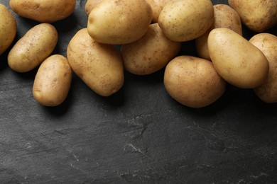 Many fresh potatoes on black textured table, above view. Space for text