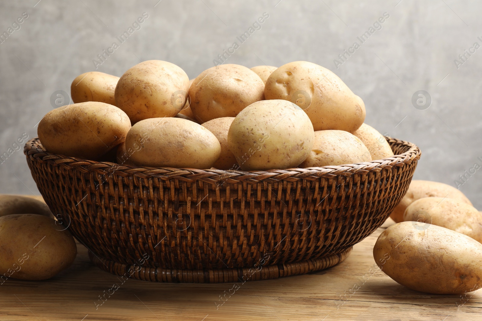 Photo of Many fresh potatoes in wicker basket on wooden table, closeup