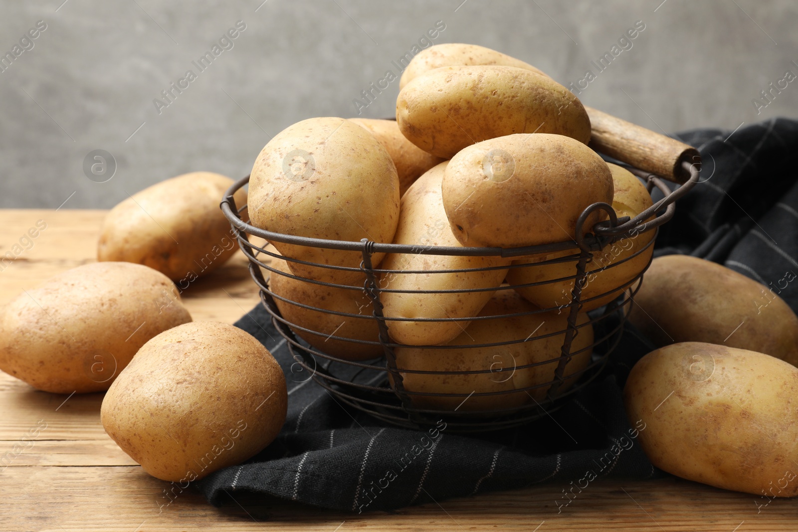 Photo of Many fresh potatoes in metal basket on wooden table, closeup