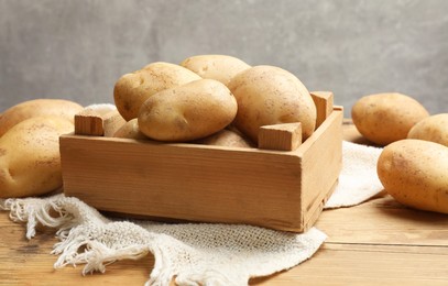 Many fresh potatoes in crate on wooden table, closeup