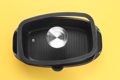 Photo of Black pot and glass lid on yellow background, top view