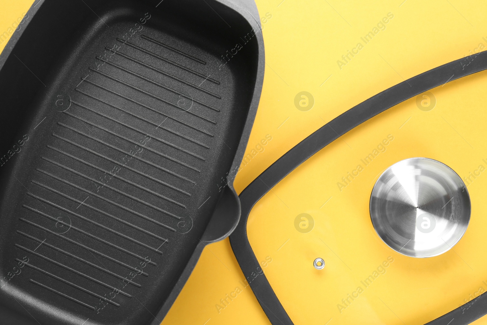 Photo of Black pot and glass lid on yellow background, top view