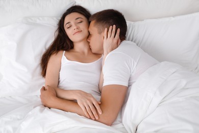 Photo of Lovely couple kissing in bed at home, top view