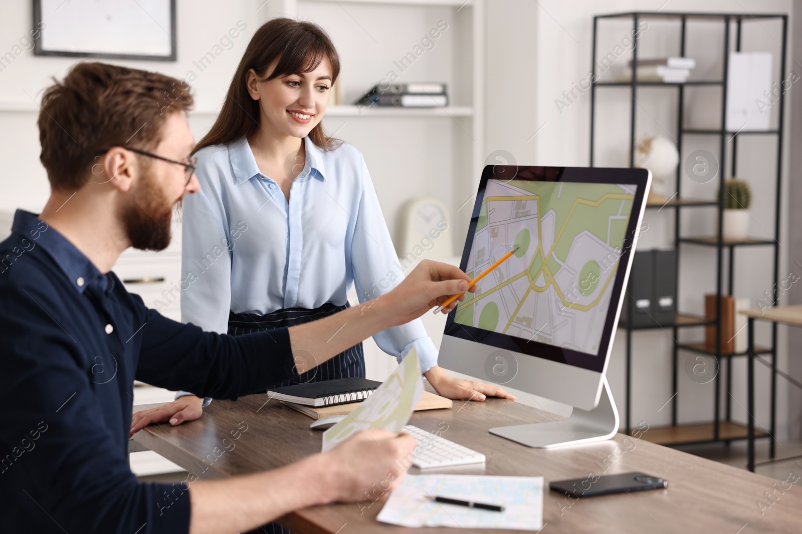 Photo of Cartographers working with cadastral map on computer at table in office