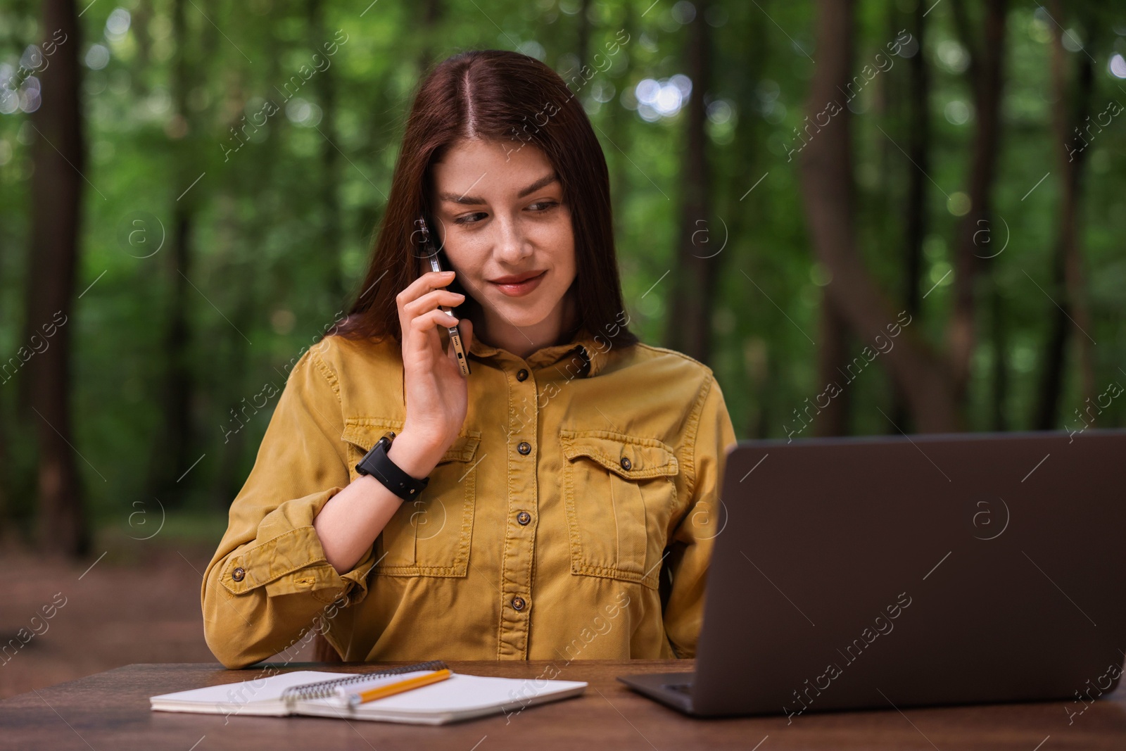 Photo of Freelancer talking on smartphone at table with laptop outdoors. Remote job