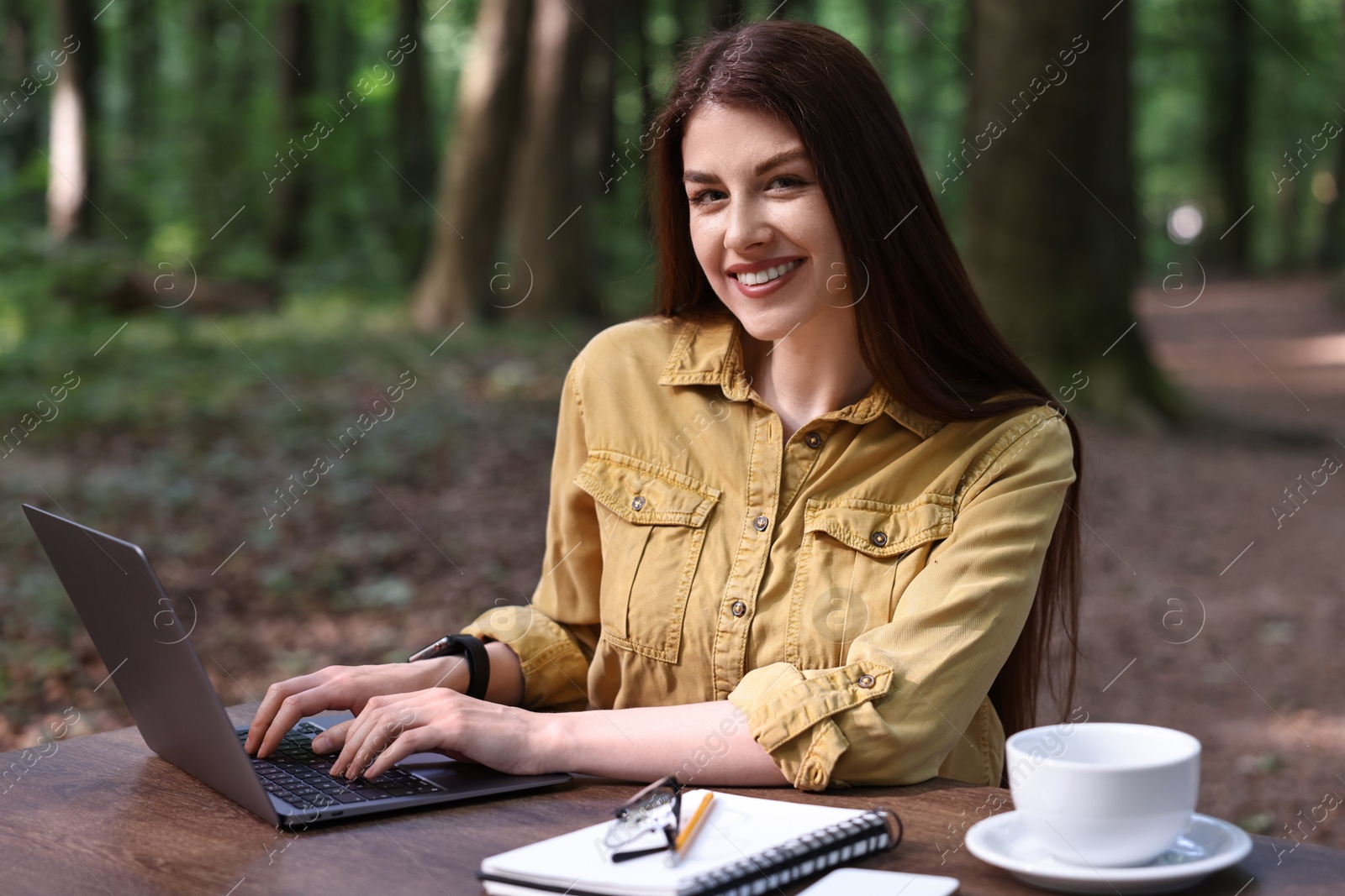 Photo of Smiling freelancer working with laptop at table outdoors. Remote job