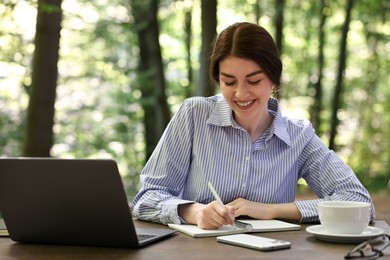 Smiling businesswoman writing something at table outdoors. Remote work