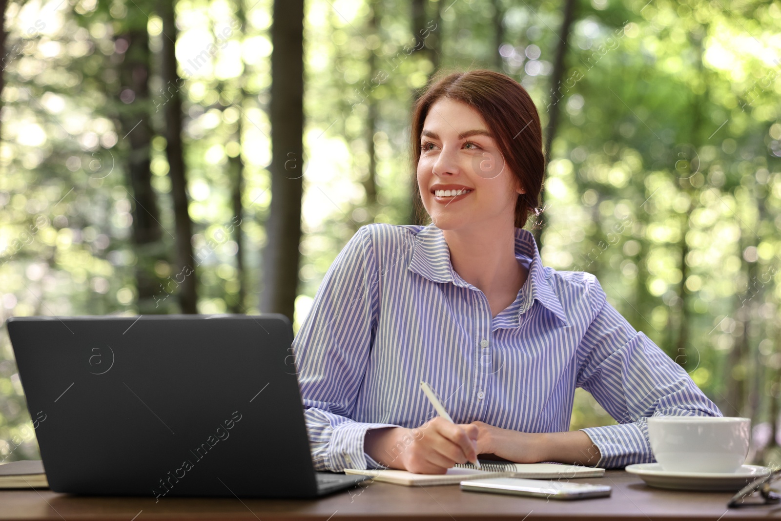 Photo of Smiling businesswoman writing something at table outdoors. Remote work