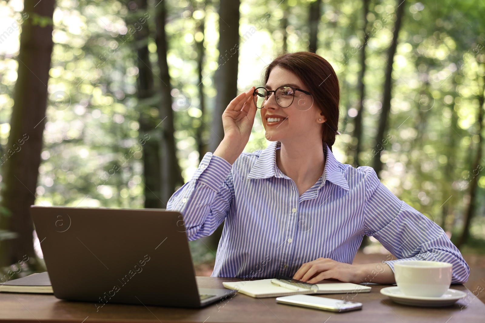 Photo of Smiling businesswoman working with laptop at table outdoors. Remote job