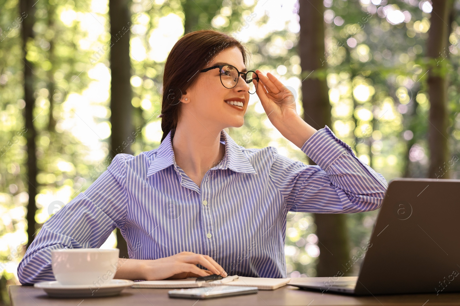 Photo of Smiling businesswoman working with laptop at table outdoors. Remote job