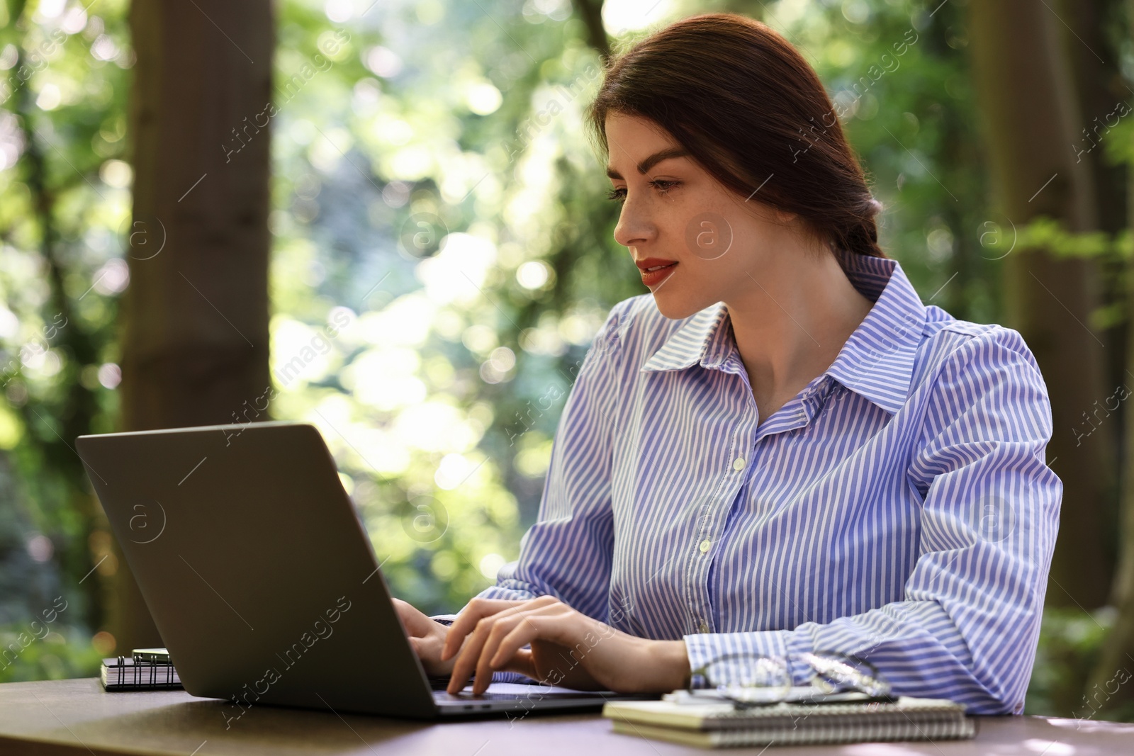 Photo of Businesswoman working with laptop at table outdoors. Remote job