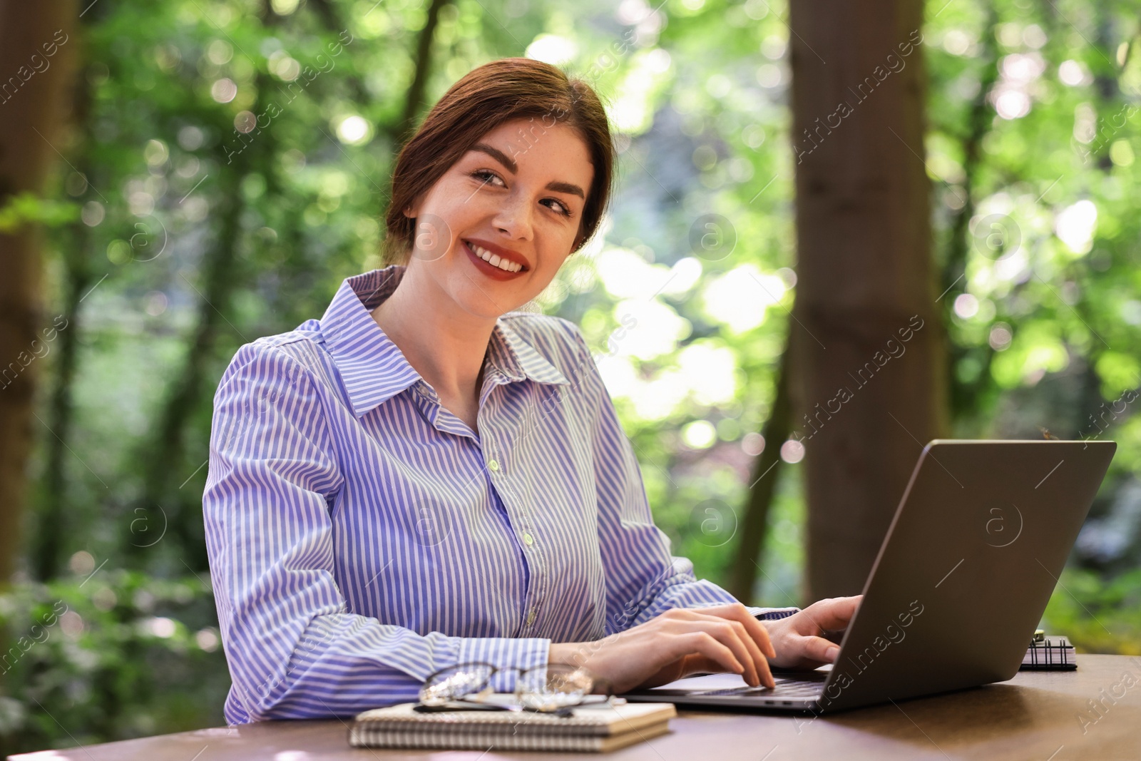 Photo of Smiling businesswoman working with laptop at table outdoors. Remote job