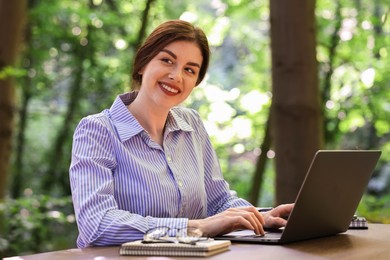 Smiling businesswoman working with laptop at table outdoors. Remote job