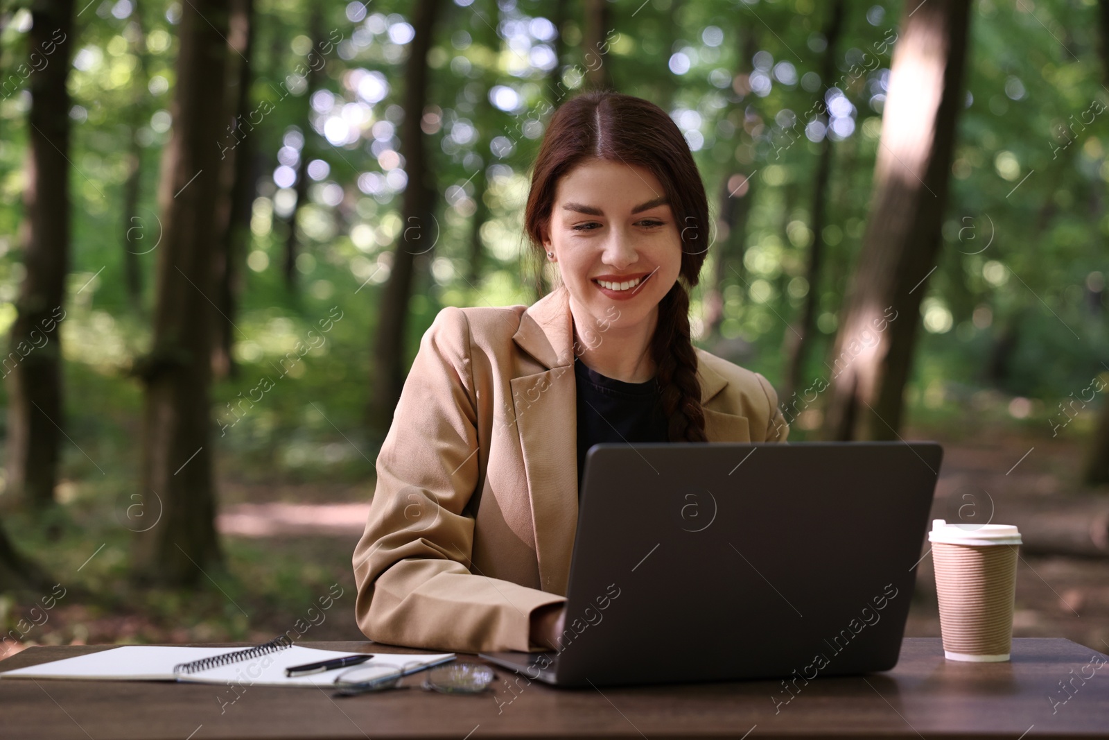 Photo of Smiling businesswoman working with laptop at table outdoors. Remote job