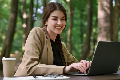 Smiling businesswoman working with laptop at table outdoors. Remote job