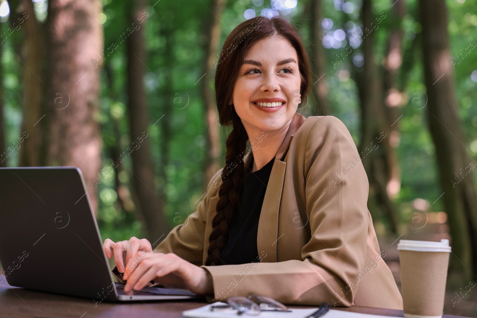 Photo of Smiling businesswoman working with laptop at table outdoors. Remote job