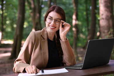 Smiling businesswoman working with laptop at table outdoors. Remote job