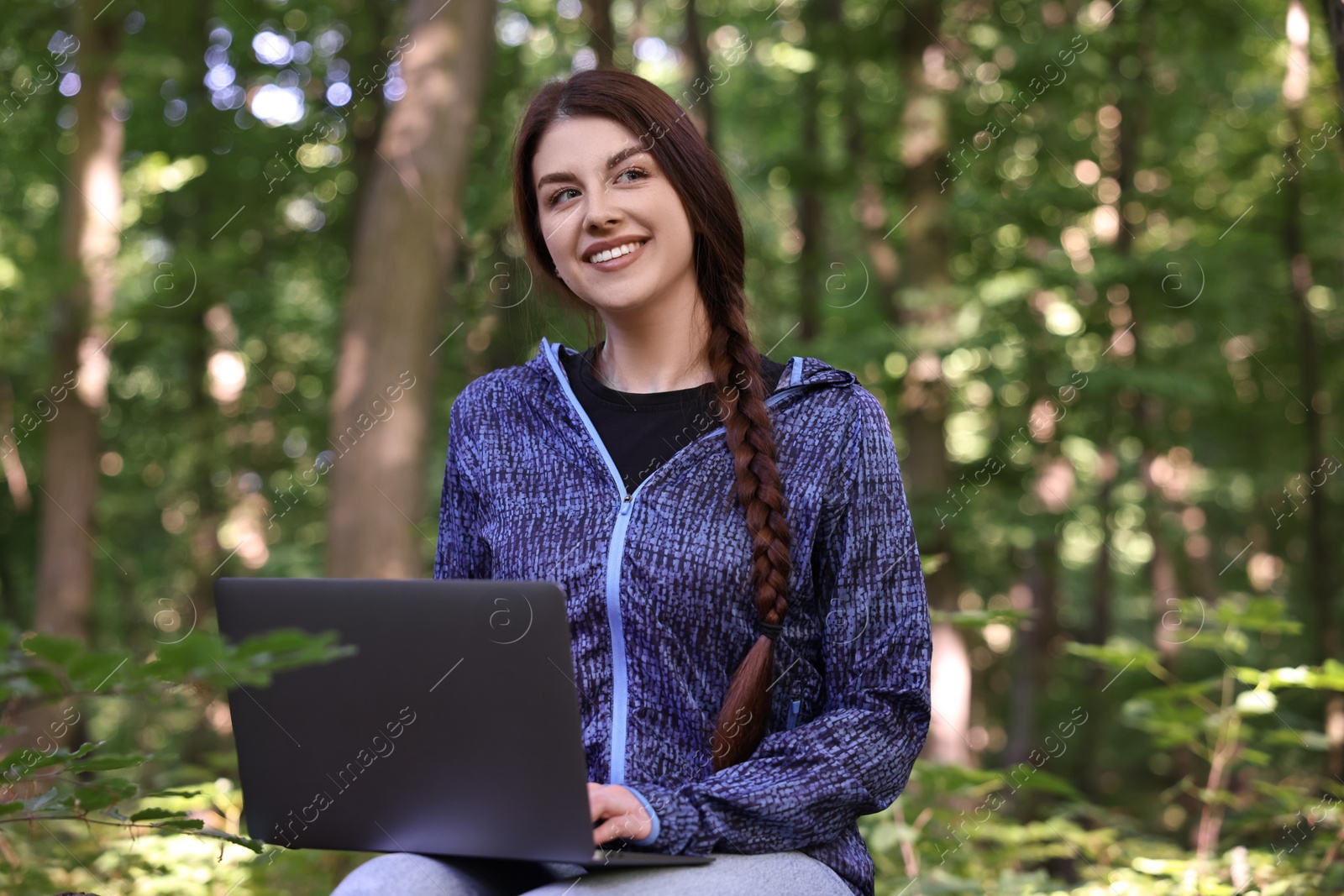 Photo of Smiling freelancer working with laptop in forest. Remote job