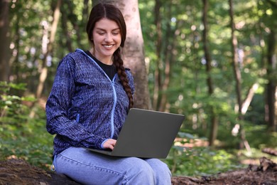 Smiling freelancer working with laptop in forest, space for text. Remote job