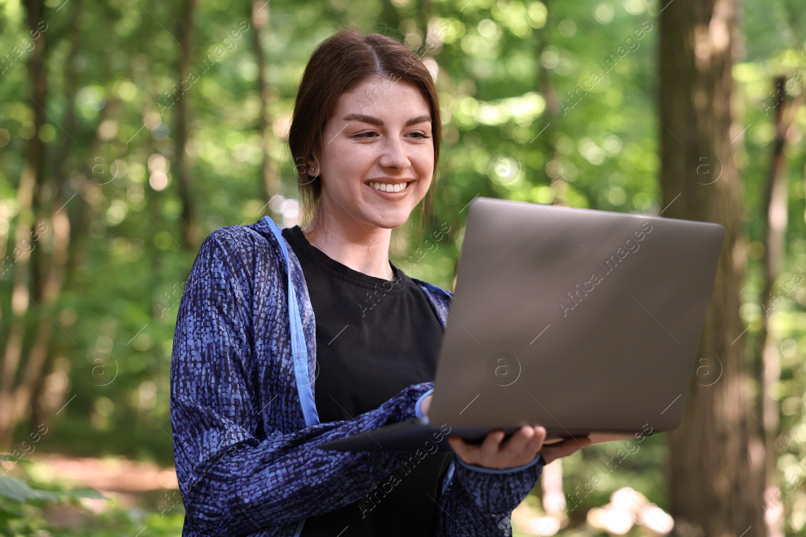 Photo of Smiling freelancer working with laptop in forest. Remote job