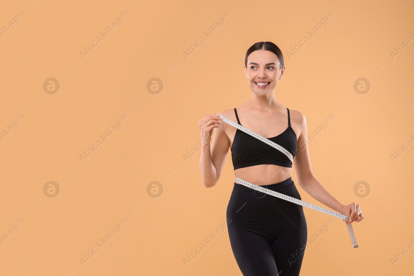 Photo of Diet and weight loss concept. Woman with measuring tape showing her slim body against beige background. Space for text