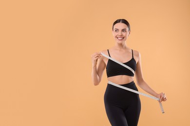 Photo of Diet and weight loss concept. Woman with measuring tape showing her slim body against beige background. Space for text