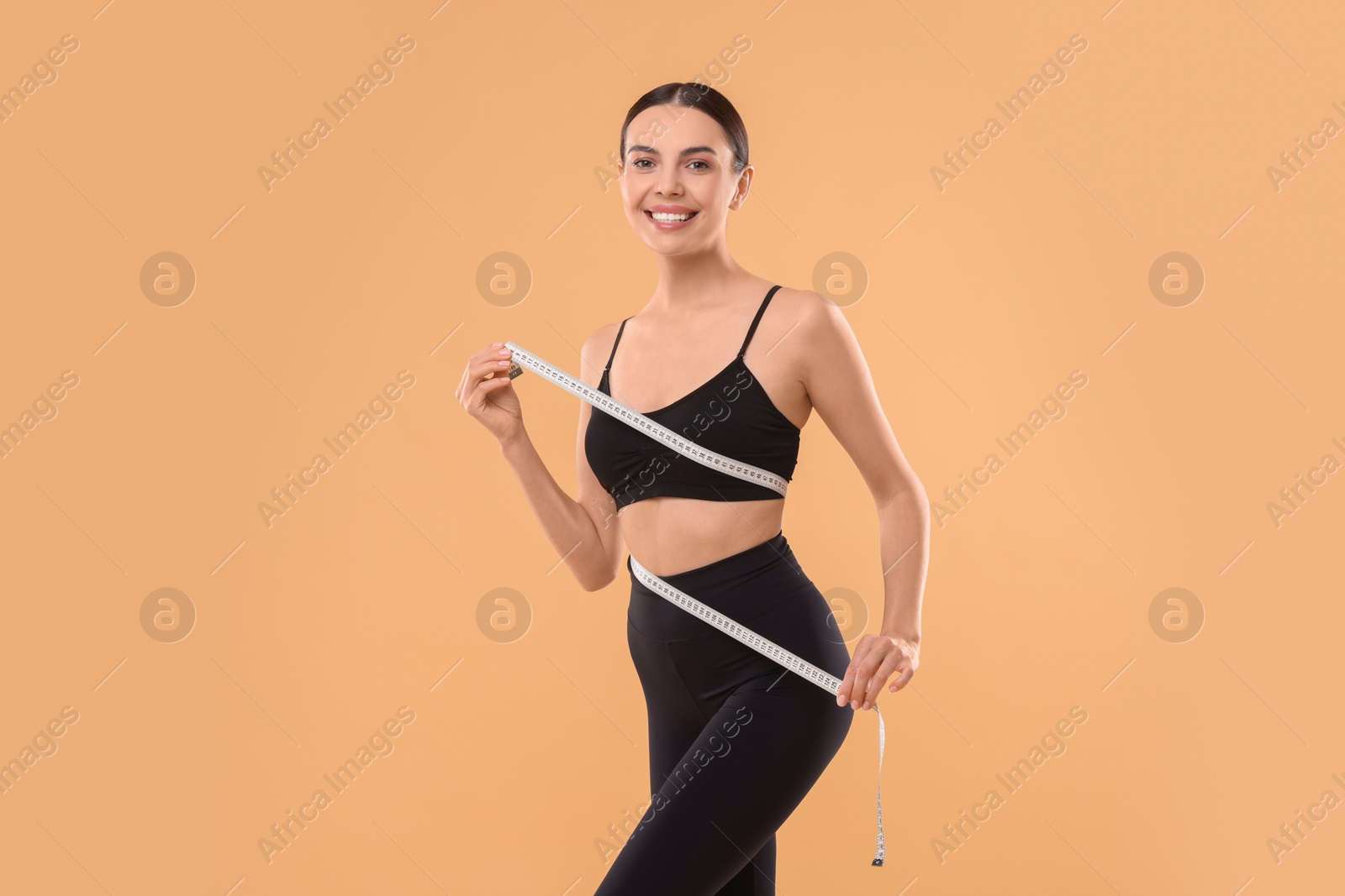 Photo of Diet and weight loss concept. Woman with measuring tape showing her slim body against beige background