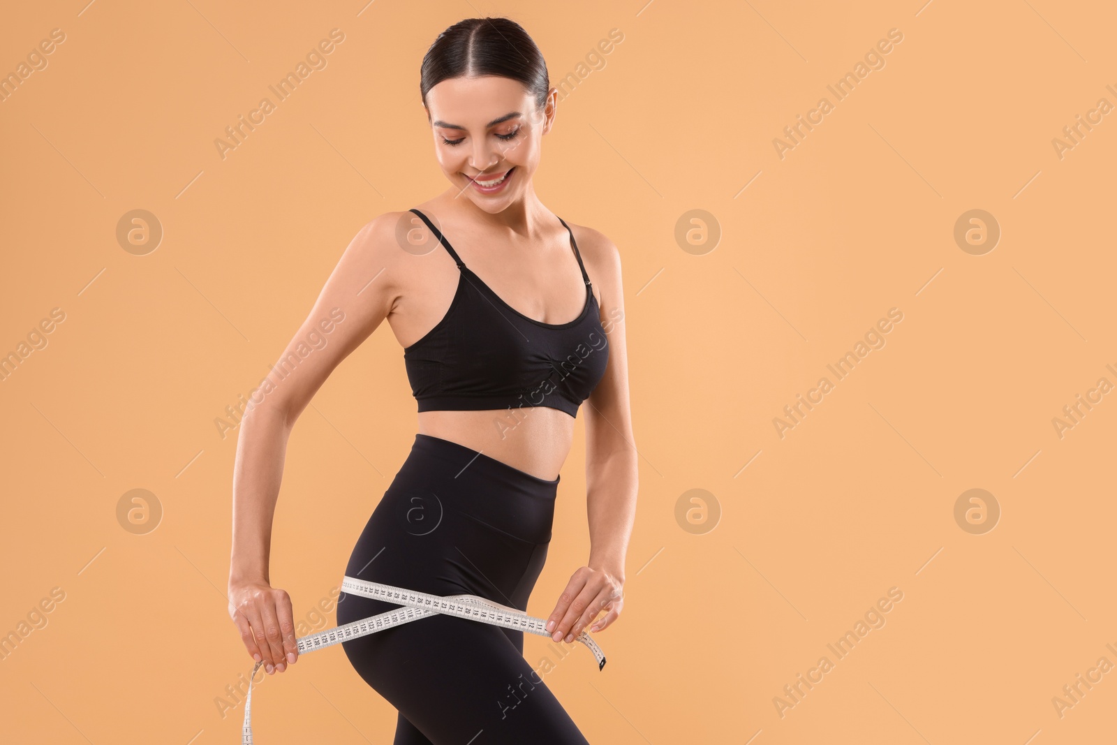 Photo of Diet and weight loss concept. Woman with measuring tape showing her slim body against beige background. Space for text