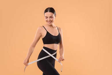 Photo of Diet and weight loss concept. Woman with measuring tape showing her slim body against beige background. Space for text