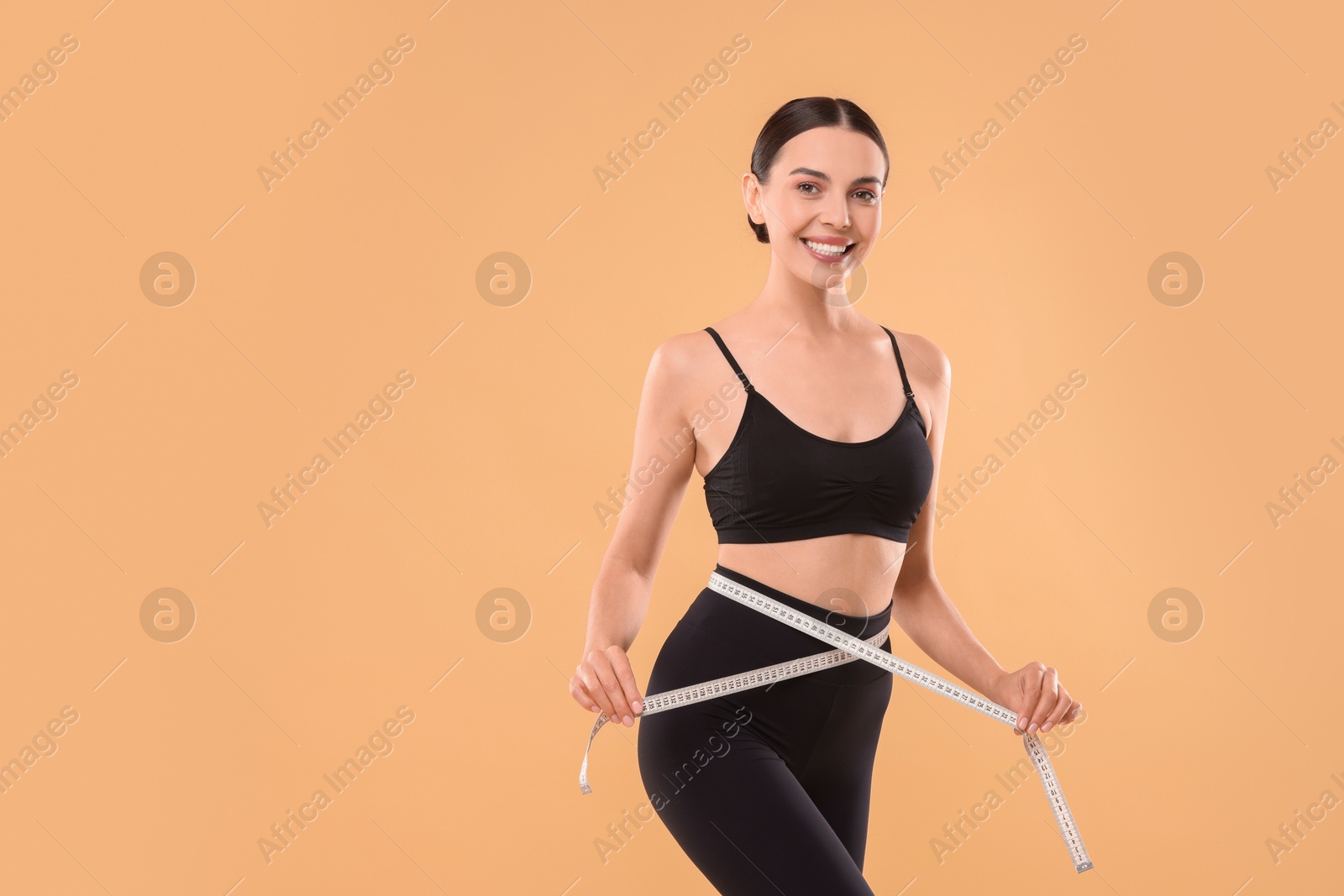 Photo of Diet and weight loss concept. Woman with measuring tape showing her slim body against beige background. Space for text