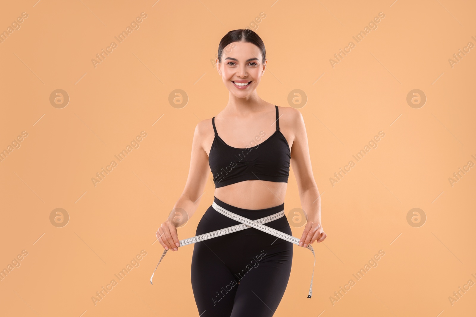 Photo of Diet and weight loss concept. Woman with measuring tape showing her slim body against beige background