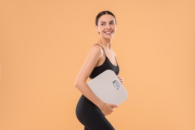 Photo of Diet and weight loss concept. Happy young woman with floor scale on beige background