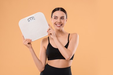 Diet and weight loss concept. Happy young woman with floor scale on beige background