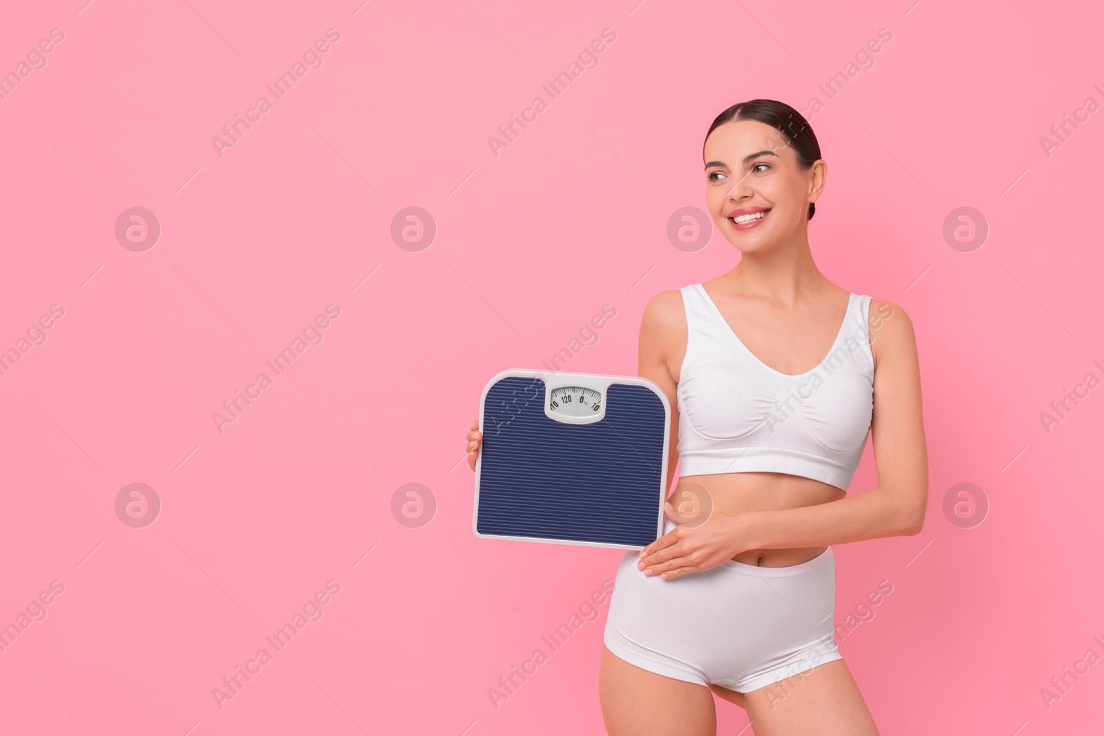 Photo of Diet and weight loss concept. Happy young woman with floor scale on pink background. Space for text